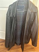Front view of the black leather jacket hanging open, showing the interior quilted lining and Tommy Hilfiger brand label on the inner neck area.