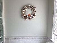 Photo of sea shell wreath hanging on wall, featuring various small shells circles in a ring shape
