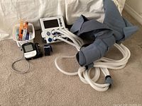 Photo showing medical devices including an electronic blood pressure monitor, pulse oximeter, pulse rate monitor, and Tactile Medical Flexitouch compression system with blue padded garments and multiple white tubes.