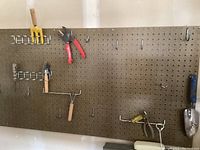Pliers and garden tools hanging on a perforated board, including small rake, trowel, pliers, wire cutters.