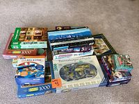 Photo showing assortment of puzzle boxes stacked on carpet. Multiple 1000 piece puzzles, a 2000 piece Ravensburger puzzle, a 500 piece Springbok puzzle, and a Roll & Stow puzzle tray.