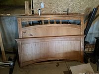 Queen size wooden bed frame parts visible: headboard, footboard, side rails in basement setting