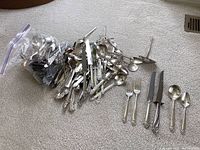 Large mixed pile and zipper bag of loose sterling flatware on carpet