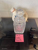 Front view of square crystal decanter with stopper on stovetop, Bohemia sticker visible, includes handwritten pink note indicating it is a whiskey decanter.