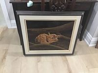 Framed painting of a resting fawn with signature visible, placed on wooden floor.