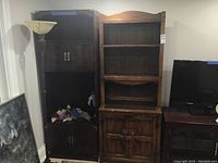 Full view of wood cabinet in room next to other furniture items, showing tall cabinet with two doors at bottom and open shelves above, scratches visible on surface.