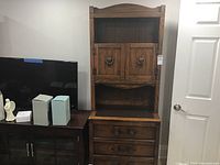 Full view of the tall wood cabinet showing its height, multiple drawers at the bottom, open mid shelf, and upper cabinet with doors and ring handles.
