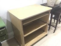 Front view of light wood manufactured wood cabinet with two shelves and one pull-out shelf, sitting on rollers.