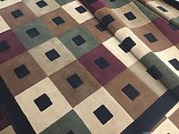 Carpet with visible multicolor square pattern, edge and fold shown.