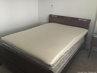 Full view of wooden double bed with mattress topper covering mattress and box spring, showing size and overall condition.