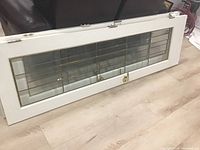 Full view of the white wood French door laying flat on the floor showing decorative glass panel and brass lock hardware.