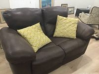 Brown faux leather love seat with two yellow geometric pattern decor pillows, showing front view.