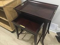 Full view of two wooden nesting tables, larger with removable tray on top, stacked together indoors.