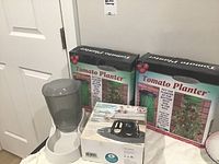 Photo showing two boxed tomato planters, a pet feeder dispenser, and the RoboMop box on a flat surface.