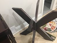 Wooden table base side view showing intersecting wide planks with dark brown finish.