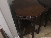 Vintage wooden side table with shaped top, turned legs, and lower shelf, viewed from side corner showing scratches and wear.