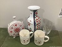 Photo showing all items in the lot: ceramic vase, round ceramic decanter with stopper, clear crystal glass, and two vintage white mugs with cabin illustration.