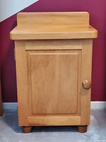 Front view of pine bedside table/cabinet showing wood grain and door with wooden knob.
