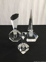 Front view of three vintage crystal perfume bottles with faceted designs and stoppers arranged upright on black surface.