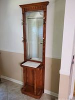 Full view of the tall wooden hall tree showing the crown molding, mirror, coat hooks, and marble shelf.