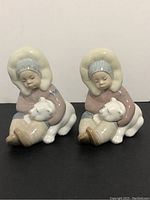 Pair of Lladro Eskimo child figurines holding polar bear cubs viewed frontally on black surface.