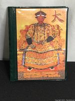 Front cover of green folding album featuring detailed colored portrait of a Qing Dynasty emperor in yellow robes, along with Chinese and English text.