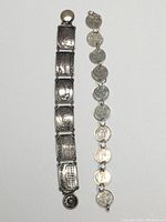 Full view of two silver-toned bracelets side by side on white background, one made of linked coins, the other made of engraved silver panels