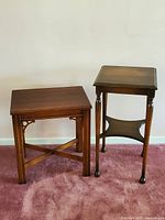 Two wooden accent tables side by side on pink carpet against a white wall showing their size and design differences