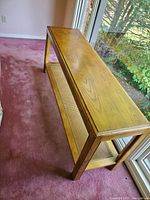 Full view of wooden sofa/console table showing wood top and cane lower shelf near window.