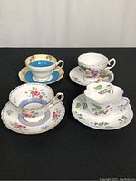 Four vintage bone china teacups and matching saucers with floral patterns, arranged on black backdrop.