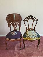 Pair of two Victorian side chairs. Both feature ornately carved wooden backs and floral needlepoint cushions in purple and green tones.