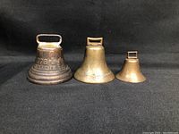 Front view of three vintage brass bells on black surface: largest bell marked 1878 Saignelegier Chiantel Fondeur, medium and small brass bells.