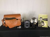 Full view of vintage Kodak Duaflex II camera, Kodak Baby Brownie Special camera with large silver flash, old cracked brown leather camera case, bulb flash, and Kodak Duaflex II pamphlet.