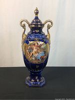 Full view of the cobalt blue lidded vase with gold handles and finial, showing the courting couple painted on front.