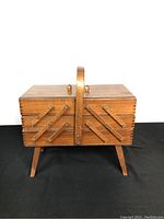 Front view of closed vintage wooden sewing box with accordion panel design and handle.