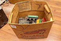 Open cardboard box containing vintage American Flyer toy train pieces including metal curved tracks, green and red train cars.