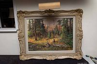Front view of ornate framed landscape painting with picture light above frame