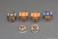 Four rolls of 12 coins each and two single coins in clear capsules, showing the original colored security bands and fronts of some coins.
