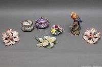 Wide view of all porcelain and figurine items arranged on table to show full lot contents including flowers, bird, and music boxes