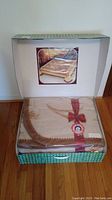 Blanket inside original packaging with clear plastic cover, red ribbon, and Coperte Pregiate medallion label visible. Cardboard box with product image at the back.