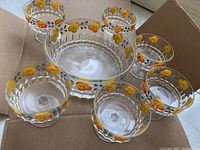 Overview of the 7 glass bowls arranged inside a cardboard box, showing the floral design and shape differences between the small and large bowls.