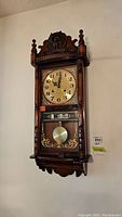 Front view of vintage wooden wall clock with pendulum displaying decorative eagle carving on top and ornate clock face with Arabic numerals.