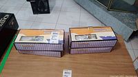 Four boxed 12-piece coffee sets on table with original packaging showing striped purple and beige pattern on box and seller auction label