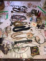 Wide shot of assorted costume jewelry including chains, bracelets, rings, earrings, and loose beads on a floral tablecloth.