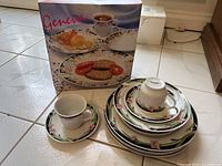 Stacked set of plates and cups next to product box showing 'Geneva' and food image