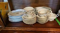 Photo showing stacked dinner plates, teacups and saucers, cream and sugar set, all with floral design and gold trim.