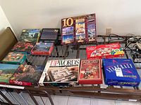 Photo showing the assortment of board games and puzzle boxes on a rack including Snakes and Ladders, Upwords, Facts in Five, Starcrazy, and several boxed jigsaw puzzles.