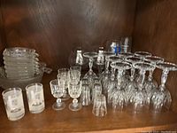 Overall view of multiple types of cut glass drinkware including glasses and ashtrays on wooden shelf.