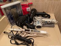 Lot of hair styling tools arranged on bathroom counter including multiple hair dryers, curling irons, and packaged items