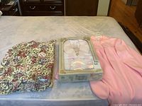 Three items displayed on bed: boxed pink fleece housecoat in original packaging, and two floral pillow shams
